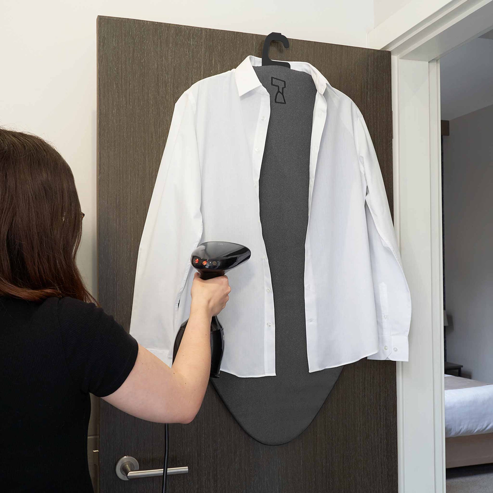 Lady using a garment steamer with Darlington mat hanging on door